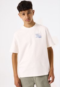 Witte katoenen t-shirt met korte mouwen, voorzien van een blauwe grafische afbeelding op de linkerborst. Eenvoudige crew neck stijl, losse pasvorm.