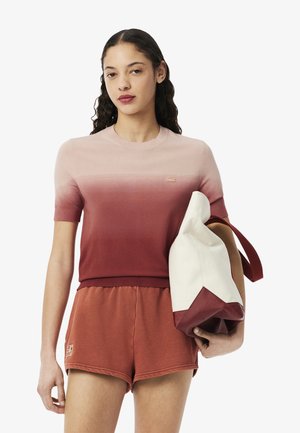 Haut en tricot à manches courtes dégradé rose à rouge, associé à un short assorti. Tient un sac bicolore en blanc et bordeaux avec des poignées en tissu.
