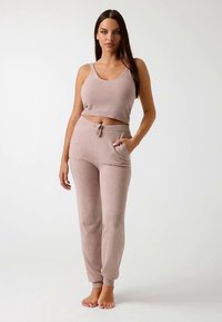 Top corto lavorato a maglia di colore rosa chiaro abbinato a pantaloni della tuta coordinati con coulisse in vita e tasche laterali. Texture liscia e vestibilità casual.