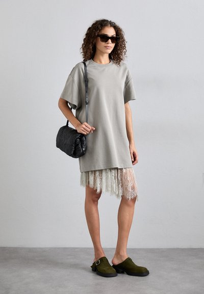 Oversized gray t-shirt dress layered over a light lace skirt, paired with black textured handbag and dark green clogs. Sunglasses complete the look.