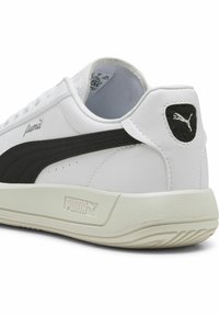 Bijela tenisica s crnim detaljima, glatka sintetika na gornjem dijelu, teksturirana potplata i Puma logo na peti. Ima podstavljeni ovratnik i jezik.