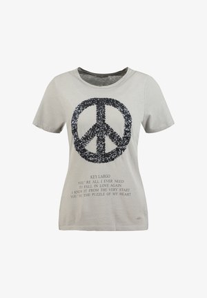 Camiseta de manga corta de color gris claro con símbolo de paz de lentejuelas negras y texto impreso con una cita sobre el amor y el rompecabezas del corazón.