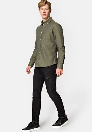 Oliwkowa, długi rękaw, koszula z guzikami z kieszonką na piersi, zestawiona z czarnymi, podartymi dżinsami i czarnymi trampkami. Gładka tekstura, dopasowany krój.