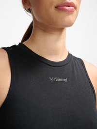 Nahaufnahme einer Person, die ein schwarzes ärmelloses Oberteil mit dem "hummel"-Logo auf der Brust trägt, wobei Hals, Lippen und ein Teil der Schulter zu sehen sind.