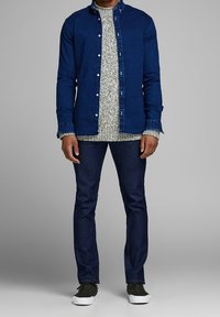 Dunkelblaues Jeanshemd über einem strukturierten, hellgrauen Pullover, kombiniert mit dunkelblauen Jeans und schwarzen Turnschuhen.