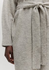 Grijze gebreide cardigan met een strikceintuur, geribbelde manchetten en een zachte, getextureerde afwerking. Heeft een losse pasvorm en mouwlengte halverwege de arm.