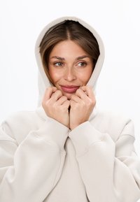 Felpa color beige chiaro con un grande cappuccio, polsini a coste e vestibilità rilassata. Il tessuto appare morbido e testurizzato, con un design minimalista.