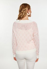 Pulover tricotat roz deschis cu un model în diamond, mansete și tiv alb cu striații și un design cu spate deschis. Purtați-l cu pantaloni albi.