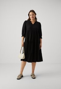 Black tiered midi dress with puff sleeves and a V-neck. Paired with beige handbag and patterned black shoes. Smooth fabric texture.