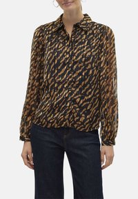 Blouse à imprimé animal noir et marron, avec des plis, des manches longues, un col et des boutons sur le devant.
