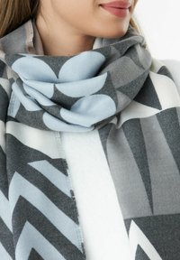 Écharpe multicolore avec des motifs géométriques gris, bleu et blanc. Tissu doux avec une texture lisse, disposée en style drapé.
