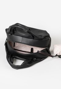 Zwarte leren handtas met een gestructureerd oppervlak, ritsluiting en een licht patroon aan de binnenzijde. Inclusief dubbele handgrepen en een afneembare schouderband.