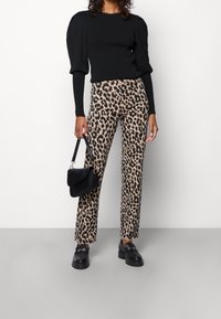 Suéter negro con mangas abullonadas, combinado con pantalones de pata de elefante beige con estampado de leopardo. Un bolso negro y unos mocasines negros gruesos completan el look.