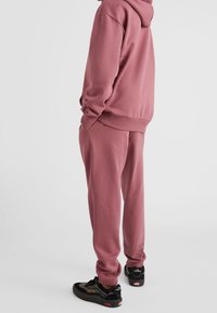 Conjunto de sudadera rosa suave y pantalones de chándal a juego, fabricado con tejido suave, que presenta un corte relajado, puños acanalados y bolsillos laterales. Zapatillas negras incluidas.