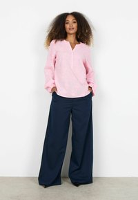 Roze geborduurde blouse met een uitsnijding aan de kraag en lange mouwen, gecombineerd met marineblauwe wijde pantalon met een gladde textuur en strakke lijnen.