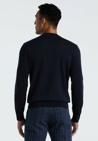 Marineblauwe gebreide trui met een ronde halslijn, geribbelde manchetten en zoom, gecombineerd met geruite broek in de kleuren blauw en wit.