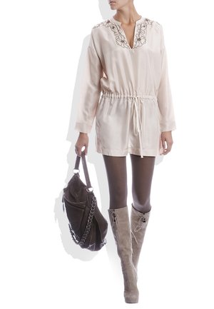 Tunique en satin rose clair avec un col en V, des broderies florales et une taille cintrée. Associée à des bottes grises arrivant au genou et à un sac à main sombre.
