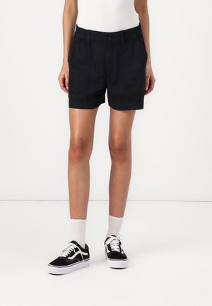 Sort bomulds shorts med elastisk talje og forlommer, parret med sorte og hvide sneakers og hvide ankelstrømper.