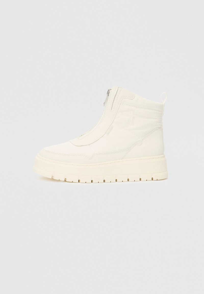 Hvit høyhælte sneakersko med glidelås på siden, tykk såle med dekk, og løftestropp bak, vist fra siden på en enkel bakgrunn.