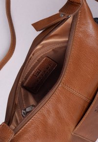 Brown leather handbag with a smooth texture, featuring a zippered compartment and an interior tag. The lining is a soft, shiny fabric.