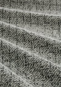 Close-up van gestructureerde stof met een zwart-wit gespikkeld patroon dat diagonaal gevouwen wordt over het oppervlak.