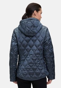 Gequilted, met capuchon, jas in donkerm blauw. Heeft een glanzende afwerking en een uniek ruitpatroon met gedetailleerde stiksels.