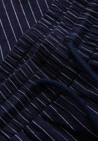 Tissu bleu foncé avec fines rayures blanches verticales et une ceinture élastique avec un cordon bleu.