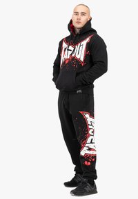 Schwarzes Hoodie- und Jogginganzug-Set mit rotem und weißem "TAPOUT"-Logo und Spritzdesign, aus weichem Stoff, mit einer Fronttasche und elastischen Bündchen.