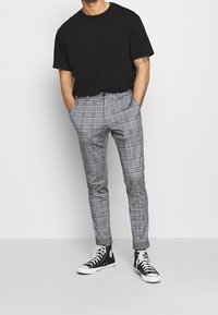 Svart kortärmad t-shirt, grå rutiga slim-fit byxor och svarta högra sneakers med schackrutig mönstring och framfickor.