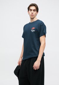 Ναυτικό μπλε T-shirt Nike από βαμβάκι, με κόκκινο λογότυπο στο στήθος και κείμενο "ΜΟΝΟ ΓΙΑ ΕΞΟΥΣΙΟΔΟΤΗΜΕΝΟ ΠΡΟΣΩΠΙΚΟ". Βραχίονες κοντοί και χαλαρή εφαρμογή.