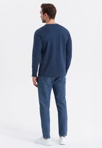 Marineblaues Langarmshirt mit Rundhalsausschnitt und kontrastierenden Besätzen, kombiniert mit hellblauen Denim-Jeans und weißen Sneakers.