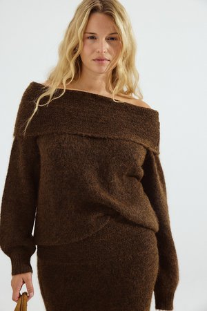 Maglione marrone off-shoulder in morbido knit testurizzato con maniche lunghe e vestibilità ampia, abbinato a un pantalone coordinato.