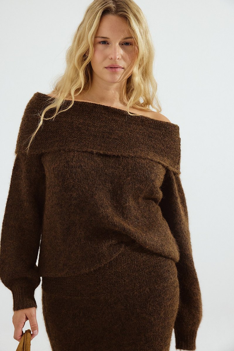 Maglione marrone off-shoulder in morbido knit testurizzato con maniche lunghe e vestibilità ampia, abbinato a un pantalone coordinato.