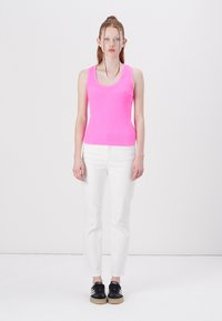 Rosa ribbet tanktopp, hvite tettsittende jeans og svarte sneakers. Topp har en rund halslinje, og jeansene har rett passform med lite stretch.