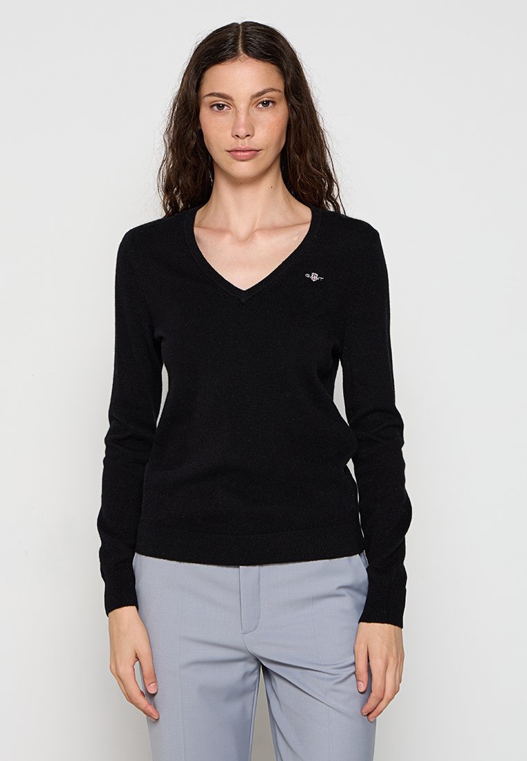 Schwarzer V-Ausschnitt-Pullover aus einem weichen Material, mit langen Ärmeln und einem kleinen gestickten Logo auf der linken Brust. Glatte Textur.