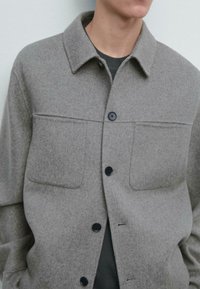 Grå uldskjortejakke med krave, to brystlommer og sorte knapper. Blød tekstur og en lige snitdesign.