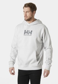 Sudadera blanca hecha de una tela suave, con un bolsillo frontal, puños acanalados y un logo de camuflaje con el texto "HELY HANSEN" en el pecho.