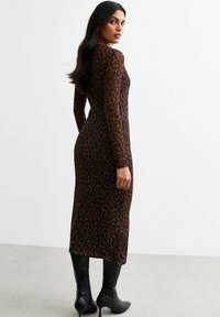 Robe ajustée à manches longues en imprimé léopard, fabriquée dans un tissu doux, présentant un col rond et une longueur mi-mollet, associée à des bottes noires jusqu'au genou.
