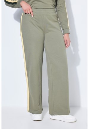 Persona che indossa pantaloni larghi verde oliva con strisce laterali gialle, indicando la vita, abbinati a scarpe da ginnastica bianche.