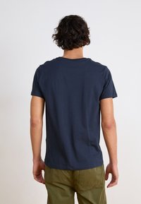Marineblå crew-neck T-skjorte laget av bomull, med korte ermer og avslappet passform, brukt sammen med grønne cargo-bukser.