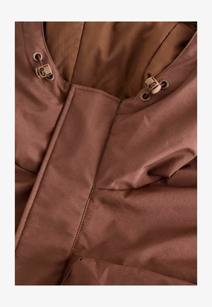 Brun isolerad jacka i tyg med en slät yta. Har en hög krage, dubbla dragsnören och quiltade designelement.