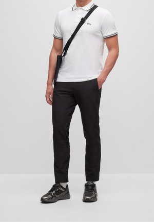 T-shirt polo blanc avec des accents noirs, pantalon slim noir et chaussures de sport noires. Comprend un petit logo sur le t-shirt.