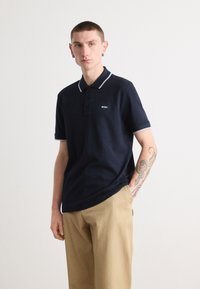 Mornarska polo majica s kontrastnim svetlo modrim ovratnikom in manšetami, z zapiranjem na tri gumbe in vezenim logotipom na prsih.