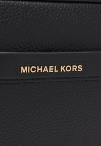Sac à main en cuir noir avec une finition texturée, présentant un logo doré "MICHAEL KORS" sur une sangle d'accent noir.