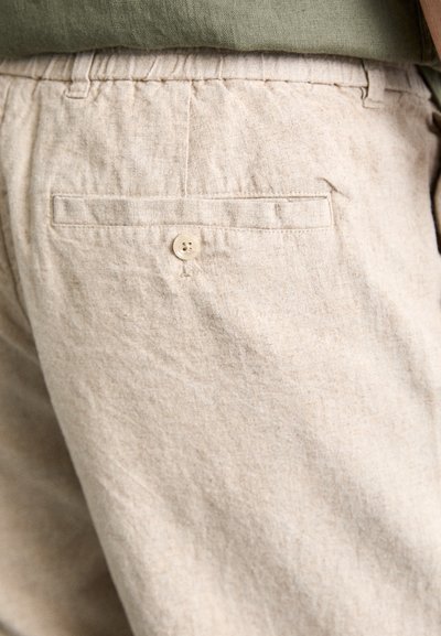 Shorts en lin beige avec une finition texturée, dotés d'une taille élastique et d'une poche arrière unique avec fermeture à bouton.