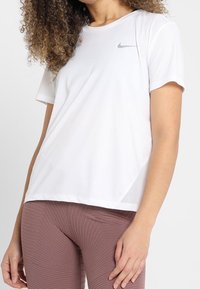 Camiseta deportiva blanca de Nike con mangas cortas, cuello redondo y sutil logotipo gris. Presenta detalles de malla para una mejor transpirabilidad.