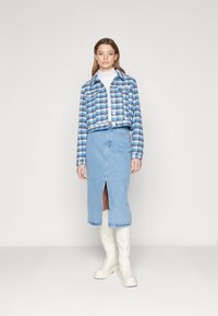 Kratka modra in bela karo jakna z dvema žepoma na prsih, kombinirana s svetlo modrim jeans mini krilom z razporkom spredaj in belimi škornji do kolen.