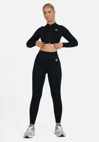 Čierny rebrovaný crop top na zips a legíny s vysokým pásom, oboje vyrobené z elastického materiálu, s malým bielym logom na hrudníku.