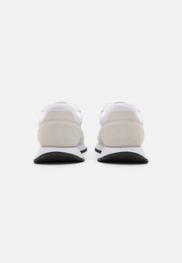 Zapatillas blancas con una parte superior sintética lisa y acentos de ante gris, con una suela de goma negra y un diseño de talón redondeado y acolchado.
