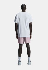 Weißes T-Shirt mit kurzen Ärmeln, kombiniert mit hellrosa Shorts. Das Outfit hat eine lockere Passform und besteht aus leichtem Stoff.